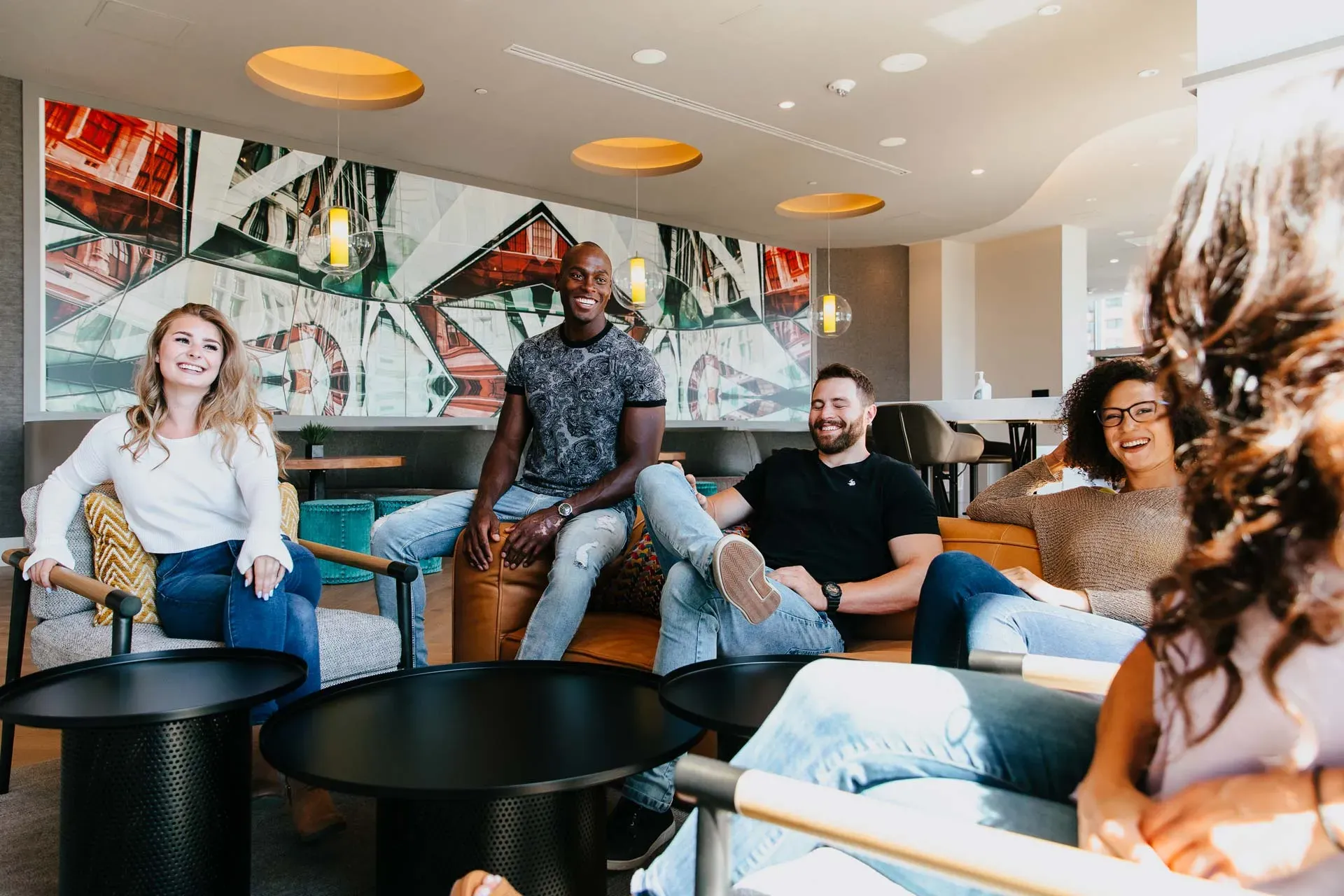 Diverse group of five people relaxing and conversing in a modern lounge area.