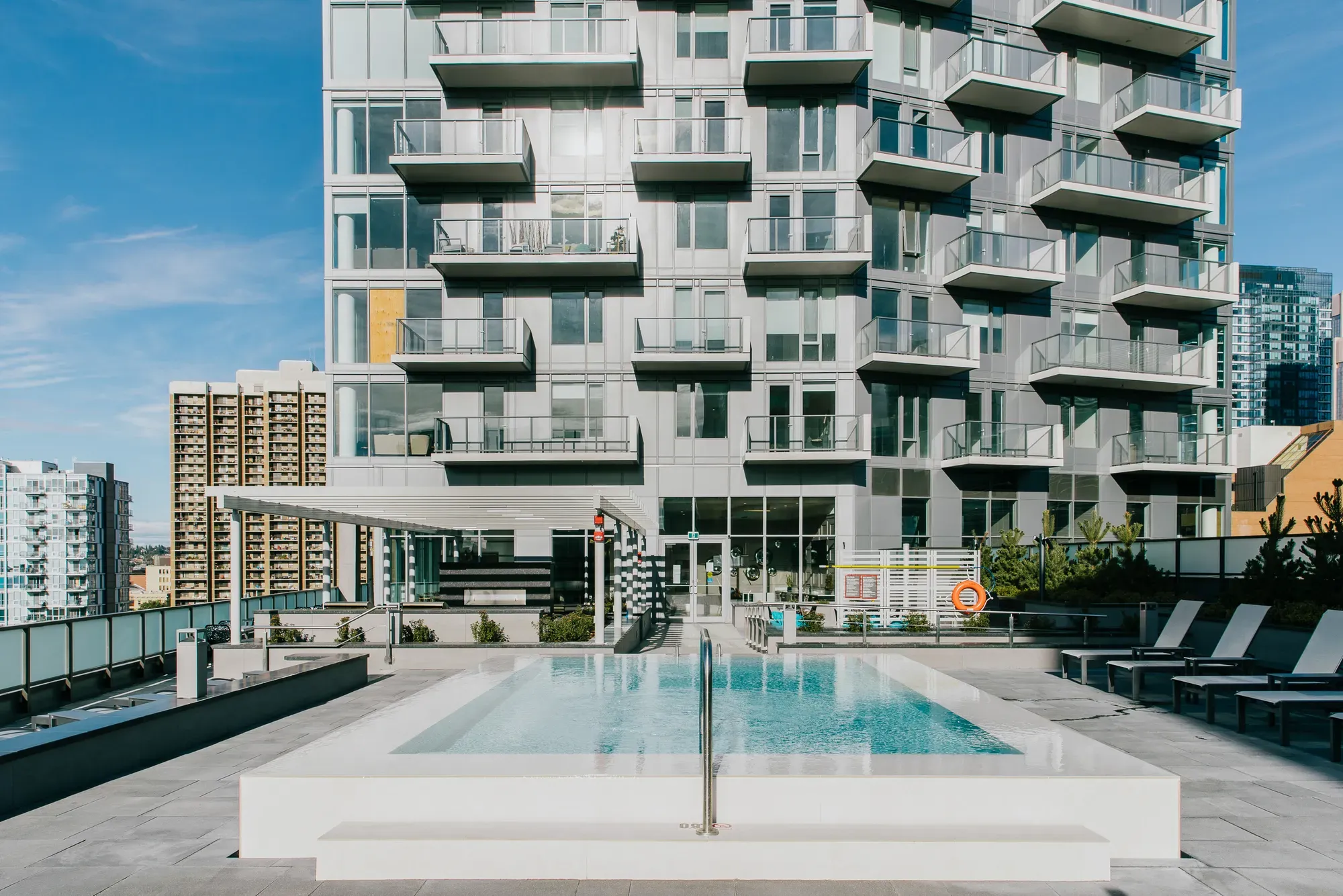 Modern building with rooftop swimming pool and lounge area under a clear sky.