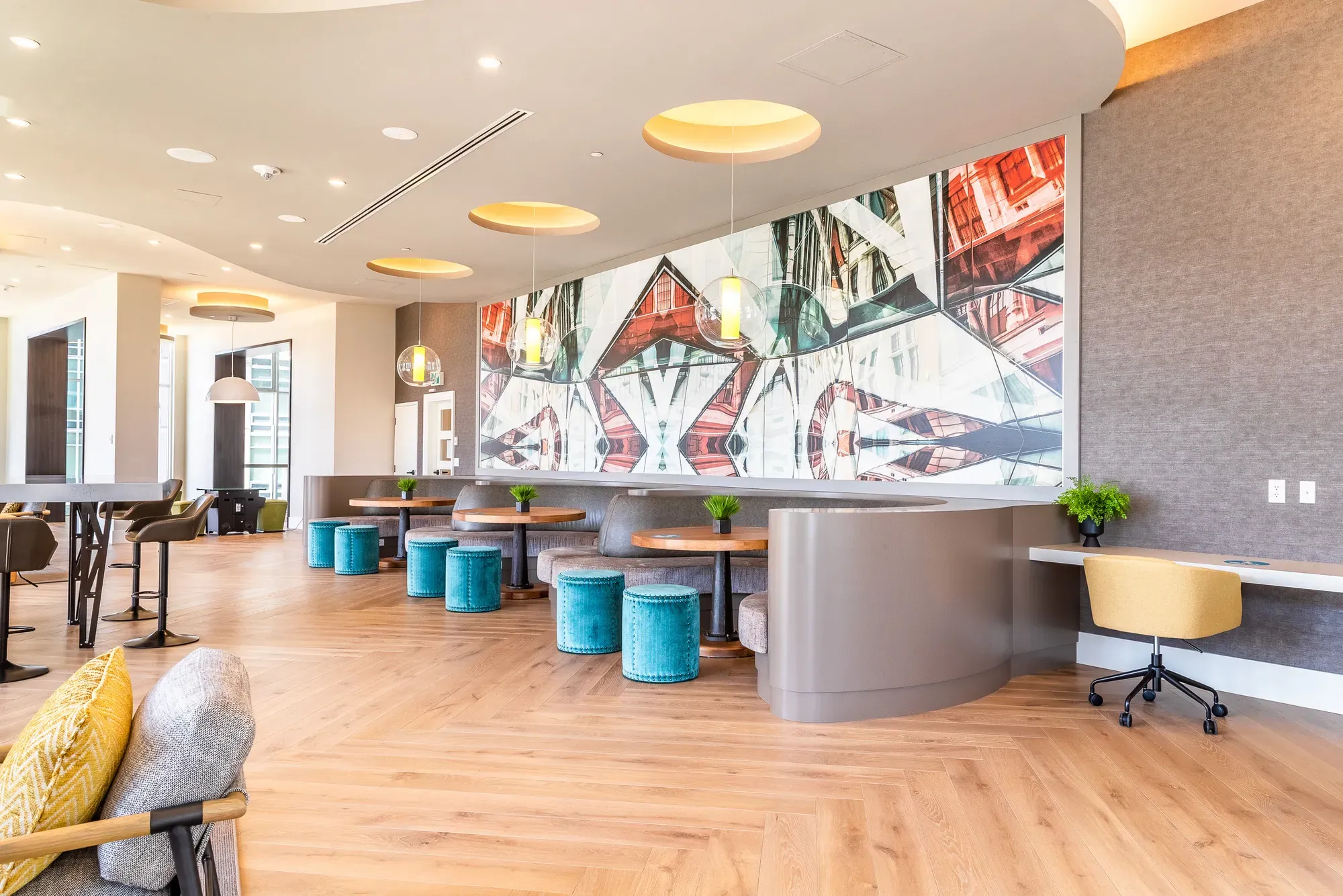 Modern lounge area with abstract mural, wood floors, and turquoise seating.