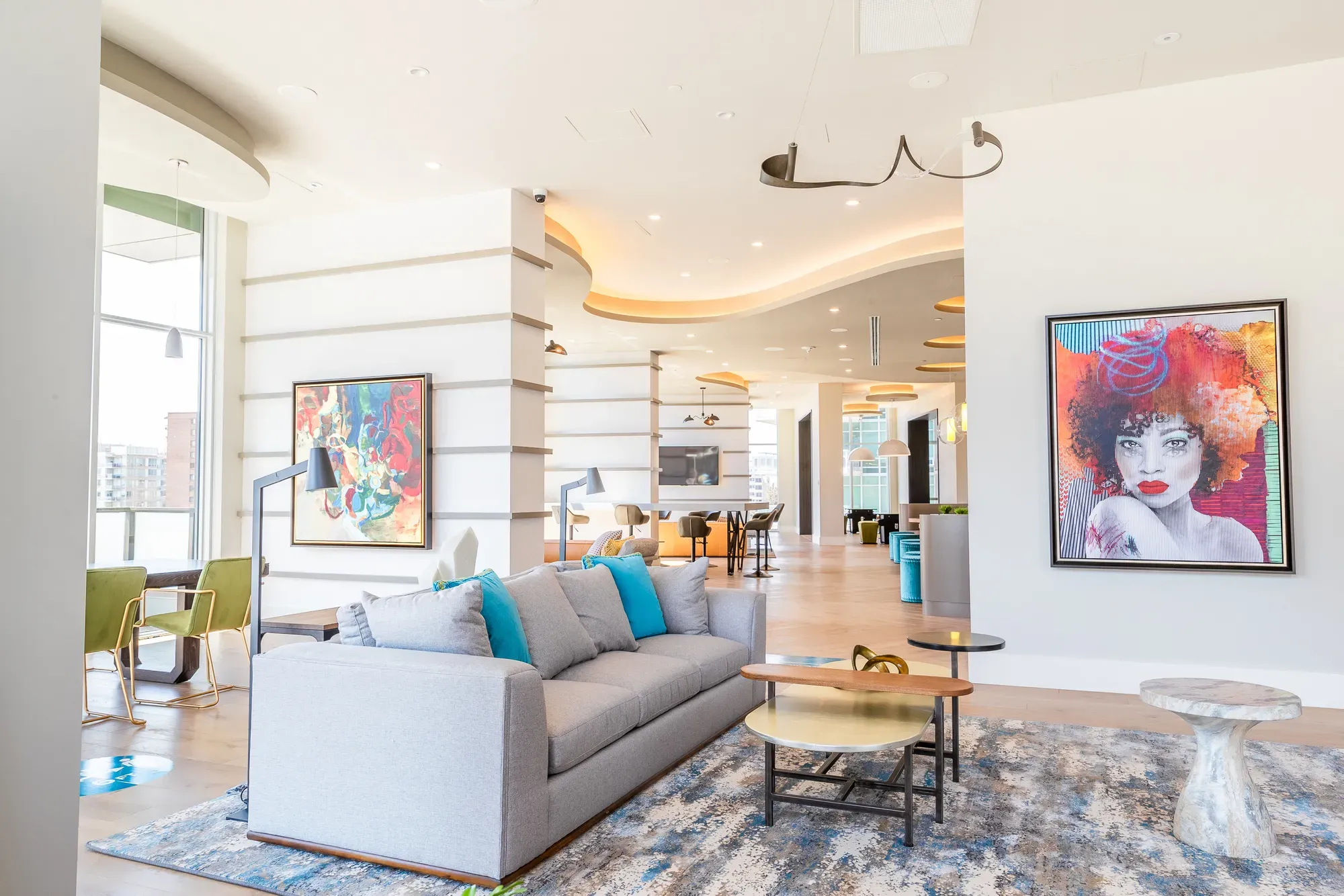 Modern lounge with a grey sofa, colorful pop art, and large windows.