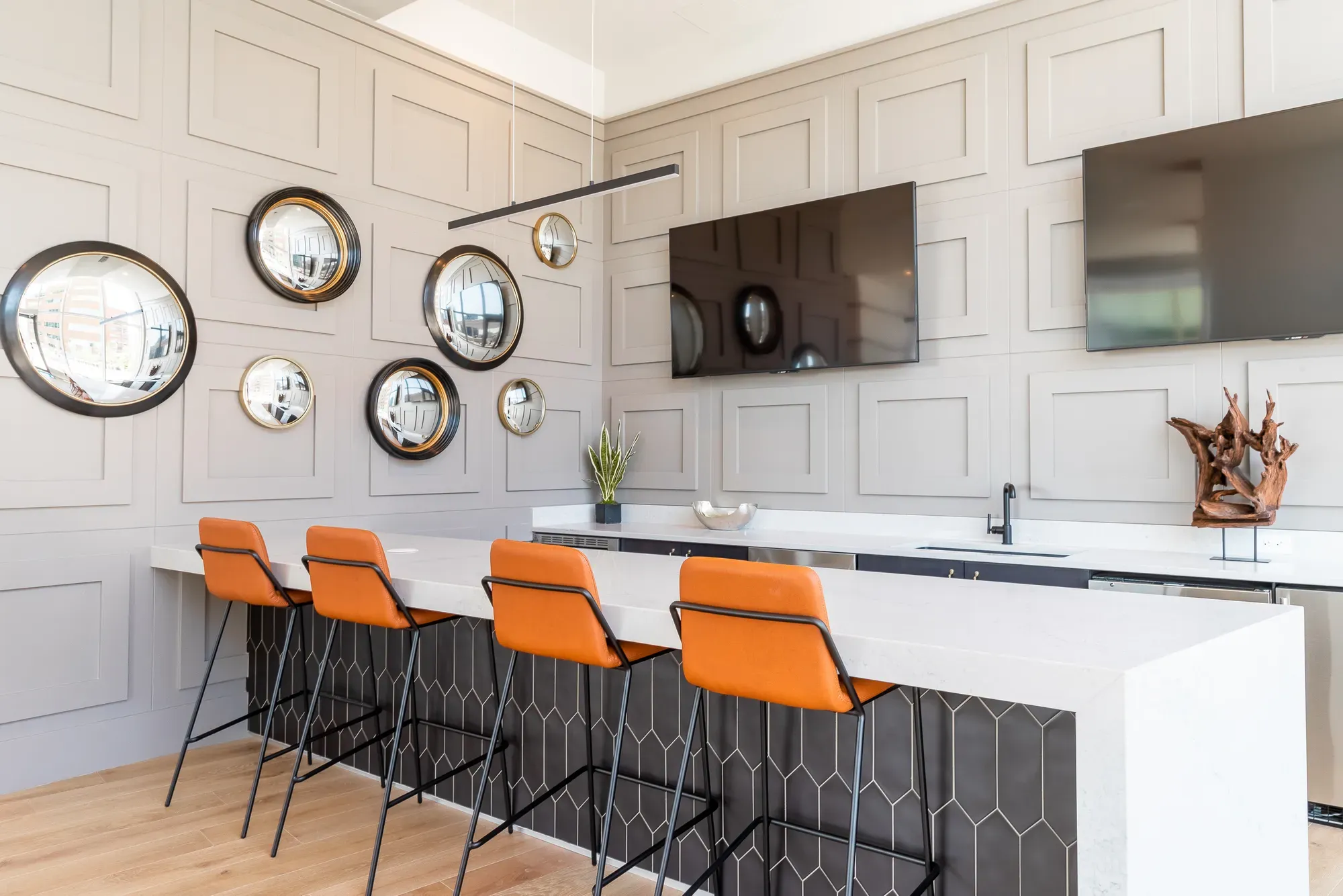 Modern lounge area with orange bar stools, circular wall mirrors, and two wall-mounted TVs.