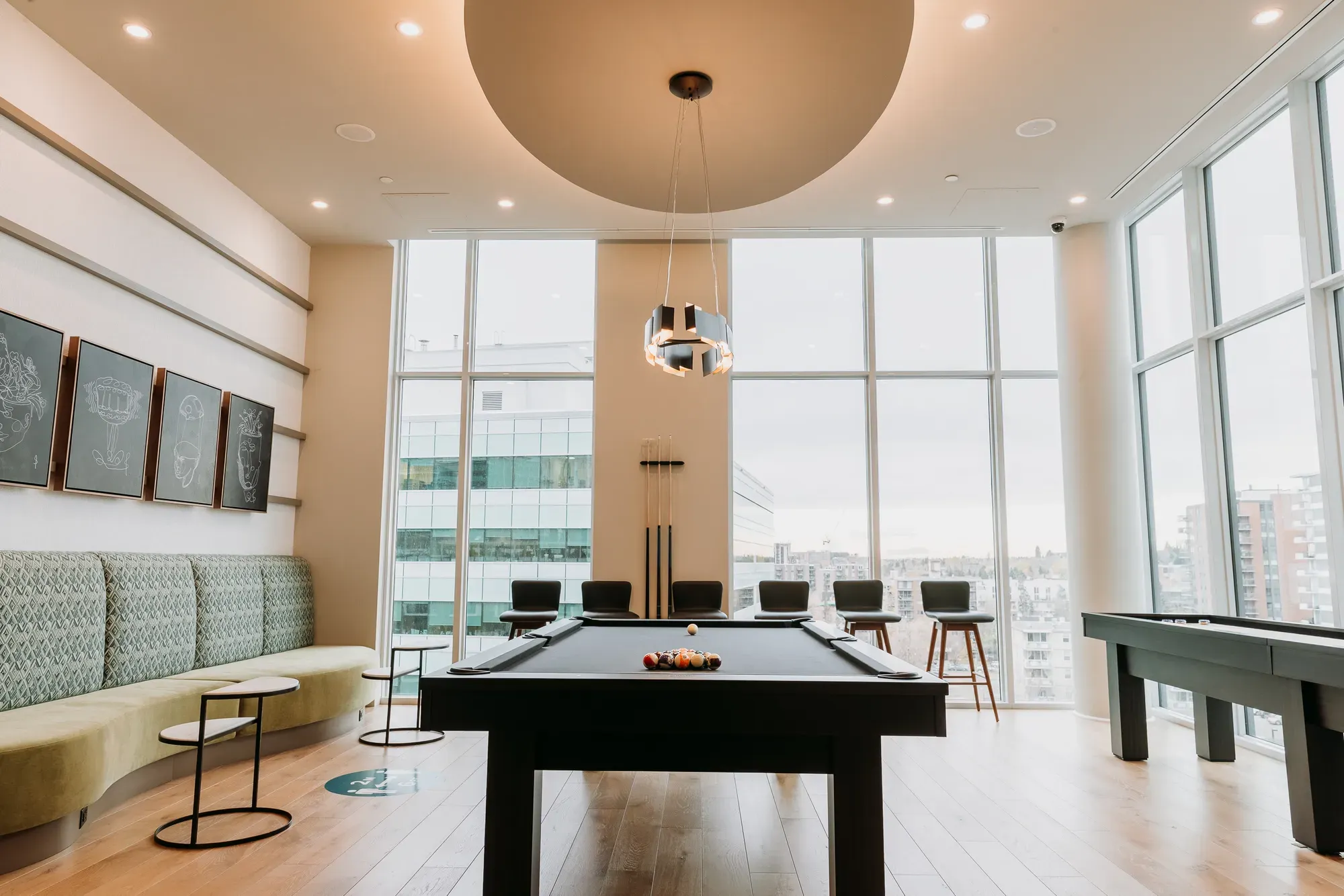 Modern game room with a pool table, curved seating, and large windows overlooking a city.